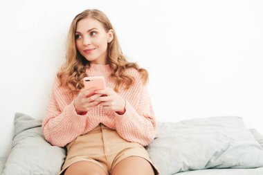 Gündelik giysiler içinde genç ve güzel bir kadın. Seksi kaygısız kadın sabahları lüks bir dairede ya da beyaz iç mekanda otel odasında yatar. Akıllı telefon ekranına bakan ateşli model, uygulamalar kullanıyor