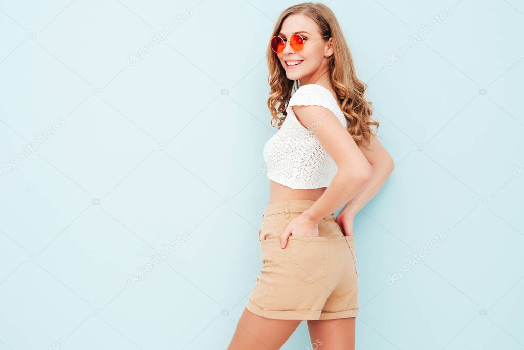 Portrait of young beautiful smiling female in trendy summer hipster suit clothes. Sexy carefree woman posing near light blue wall in studio. Positive model having fun indoors. Cheerful and happy