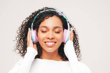 Afro kıvırcık saçlı, güzel siyah bir kadın. Kazak ve kot giyen, kablosuz kulaklıkla müzik dinleyen kaygısız bir kadın. Stüdyoda beyaz arka planda poz veriyor. Kapalı gözler.
