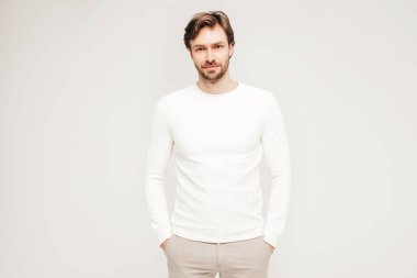 Beyaz süveter ve pantolon giyen yakışıklı, gülümseyen hippi, keresteci iş adamı modeli portresi. Stüdyoda gri arka planda poz veren modacı.