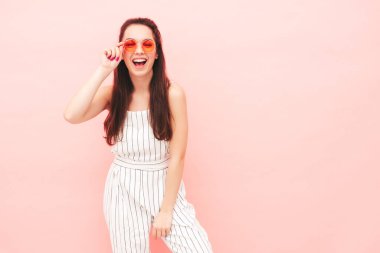 Modayı takip eden yaz hippi kıyafetleri içinde gülümseyen güzel bir kadının portresi. Stüdyoda pembe duvarın yanında poz veren kaygısız seksi kadın. Pozitif model içeride eğleniyor. Neşeli ve mutlu