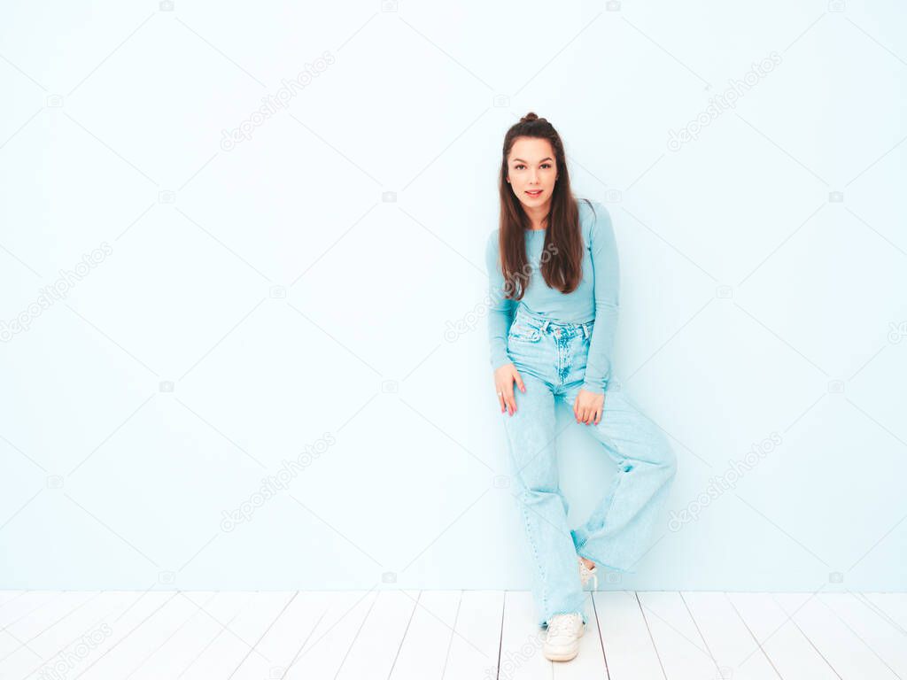 Young beautiful smiling female in trendy summer hipster clothes. Sexy carefree woman posing near light blue wall in studio. Positive model having fun indoors. Cheerful and happy 