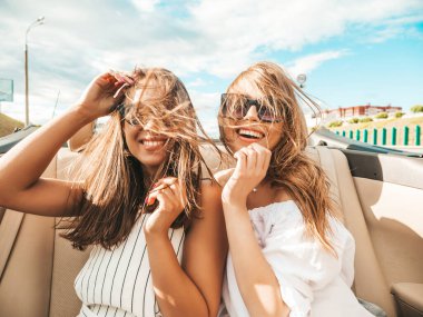 Üstü açık arabadaki iki güzel ve gülümseyen hippi kadının portresi. Cabriolet kullanan kaygısız seksi kadınlar. Pozitif modeller dışarıda güneş gözlüğü takıp eğleniyorlar. Yaz günlerinin tadını çıkarıyorlar.