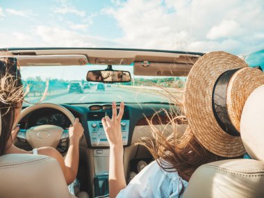 Üstü açık arabadaki iki güzel ve gülümseyen hippi kadının portresi. Cabriolet kullanan kaygısız seksi kadınlar. Pozitif modeller dışarıda güneş gözlüğü takıp eğleniyorlar. Yaz günlerinin tadını çıkarıyorlar.