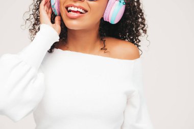 Kıvırcık saçlı, güzel siyah kadın. Süveter ve kot giyen, kablosuz kulaklıkla müzik dinleyen, kaygısız kadın. Stüdyoda beyaz arka planda poz veren.