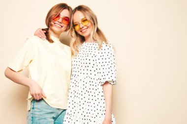 Moda kıyafetleri içinde gülümseyen iki güzel sarışın hippi kadın. Stüdyoda poz veren kaygısız seksi kadınlar. Moda ve pozitif modeller eğleniyor.