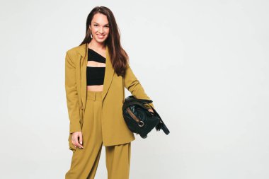 Moda kıyafetleri içinde gülümseyen genç ve güzel bir bayan. Stüdyoda gri arka planda poz veren kaygısız seksi kadın. Pozitif model içeride eğleniyor. Neşeli ve mutlu. Çanta.