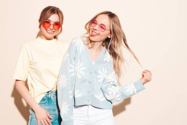 Moda kıyafetleri içinde gülümseyen iki güzel sarışın hippi kadın. Stüdyoda poz veren kaygısız seksi kadınlar. Moda ve pozitif modeller eğleniyor.