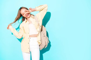 Genç ve güzel bir kadın kameraya bakıyor. Modayı takip eden kadın günlük kıyafetlerle gülümsüyor. Stüdyoda gri arka planda sırt çantalı pozlar veren pozitif ve komik bir model