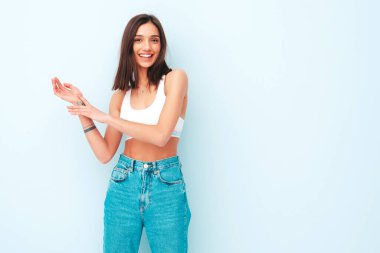 Beyaz formalı bluz ve kot pantolon giymiş güzel bir kadın. Seksi kaygısız neşeli model sabahının tadını çıkarıyor. Şirin ve pozitif kadın stüdyoda açık mavi duvarın yanında poz veriyor.