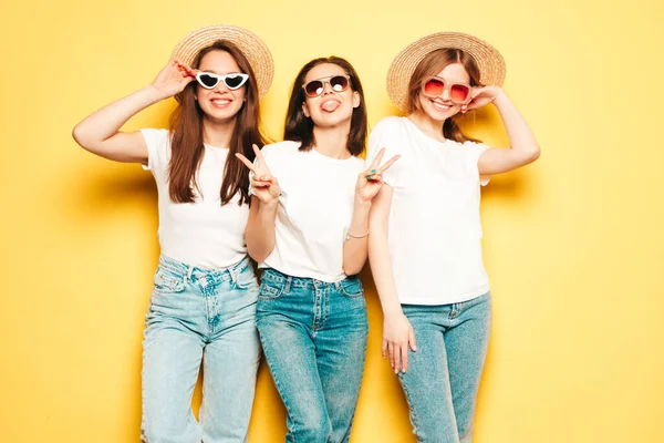 流行の夏の白いTシャツとジーンズの服を着た3人の若い美しい笑顔のヒップスター女性 スタジオで黄色の壁の近くにポーズをとるセクシーな屈託のない女性 — ストック写真