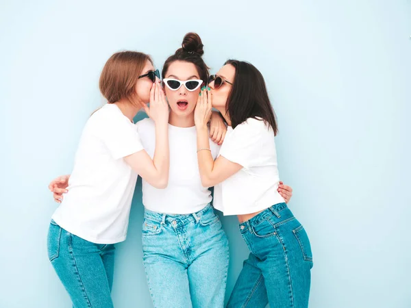 同じ夏の白いTシャツとジーンズの服で流行の3人の若い美しい笑顔のヒップスター女性 スタジオのライトブルーの壁の近くにポーズをとるセクシーな屈託のない女性 正のモデルは秘密を伝える彼らの友人 — ストック写真