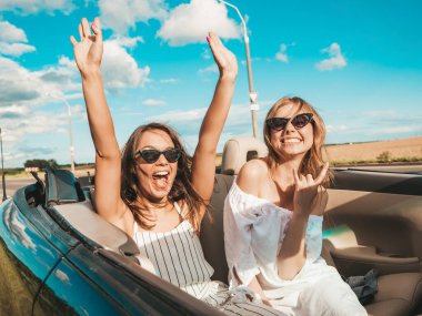 Üstü açık arabadaki iki güzel ve gülümseyen hippi kadının portresi. Cabriolet kullanan kaygısız seksi kadınlar. Pozitif modeller dışarıda güneş gözlüğü takıp eğleniyorlar. Keyifli yaz günleri