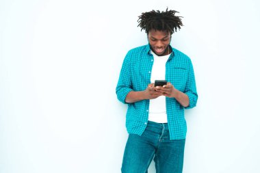 Yakışıklı, güler yüzlü, lamberseksüel model. Yaz kıyafetleri giymiş, traşsız Afrikalı adam. Stüdyoda mavi duvarın yanında poz veren, rastalı bir erkek. 