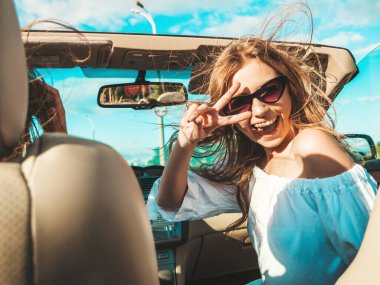 Üstü açık arabadaki iki güzel ve gülümseyen hippi kadının portresi. Cabriolet kullanan kaygısız seksi kadınlar. Pozitif modeller dışarıda güneş gözlüğü takıp eğleniyorlar. Keyifli yaz günleri