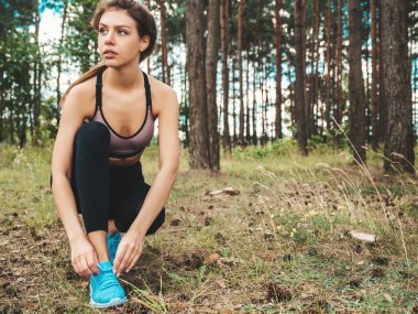 Ormanda antrenmandan önce ayakkabı bağcığı bağlayan spor bir kadın. Bayan sporcu dışarıda koşuya hazırlanıyor. Koşucu antrenmana hazırlanıyor. Spor aktif yaşam tarzı konsepti.