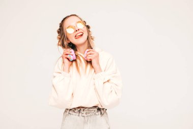 Yazlık kıyafetler giymiş güzel, gülen bir kadın. Kablosuz kulaklıkla müzik dinleyen seksi tasasız model. Stüdyoda güneş gözlükleriyle gri arka planda poz veren sevimli ve pozitif kadın.