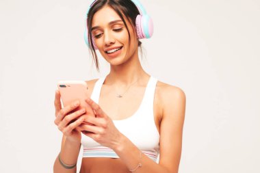 Kot pantolon giymiş, gülümseyen güzel bir kadın. Kablosuz kulaklıkla müzik dinleyen seksi tasasız model. Stüdyoda gri arka planda poz veren sevimli ve pozitif bir kadın. Akıllı telefon tutuluyor