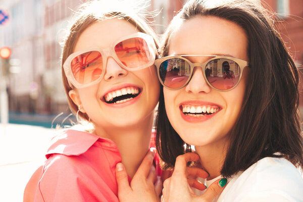 Две молодые красивые улыбающиеся женщины-хипстеры в трикотажных летних белых футболках и джинсах. Позитивные модели веселятся, обнимаются и сходят с ума