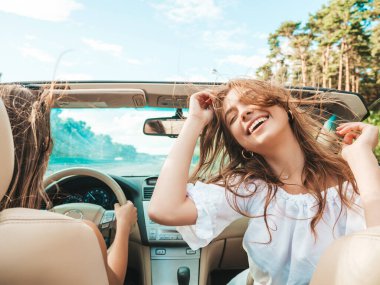 Üstü açık arabadaki iki güzel ve gülümseyen hippi kadının portresi. Cabriolet kullanan kaygısız seksi kadınlar. Pozitif modeller dışarıda güneş gözlüğü takıp eğleniyorlar. Keyifli yaz günleri