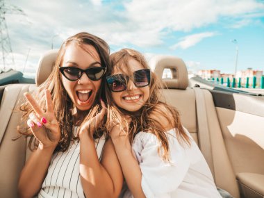 Üstü açık arabadaki iki güzel ve gülümseyen hippi kadının portresi. Cabriolet kullanan kaygısız seksi kadınlar. Pozitif modeller dışarıda güneş gözlüğü takıp eğleniyorlar. Keyifli yaz günleri