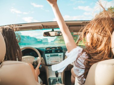 Üstü açık arabadaki iki güzel ve gülümseyen hippi kadının portresi. Cabriolet kullanan kaygısız seksi kadınlar. Pozitif modeller dışarıda güneş gözlüğü takıp eğleniyorlar. Keyifli yaz günleri