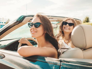 Üstü açık arabadaki iki güzel ve gülümseyen hippi kadının portresi. Cabriolet kullanan kaygısız seksi kadınlar. Pozitif modeller dışarıda güneş gözlüğü takıp eğleniyorlar. Keyifli yaz günleri