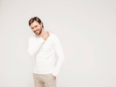 Beyaz süveter ve pantolon giyen yakışıklı, gülümseyen hippi, keresteci iş adamı modeli portresi. Stüdyoda gri arka planda poz veren modacı.
