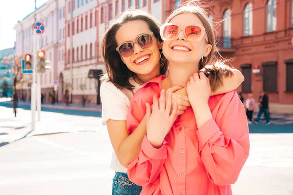 Son moda beyaz tişörtlü ve kot pantolonlu iki güzel, gülümseyen yeniyetme bayan sokak arka planında poz veren kaygısız kadınlar. Pozitif modeller eğleniyor, sarılıyor ve deliriyor.