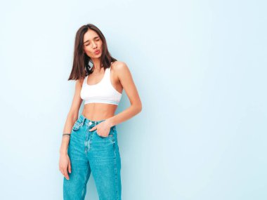 Beyaz formalı bluz ve kot pantolon giymiş güzel bir kadın. Seksi kaygısız neşeli model sabahının tadını çıkarıyor. Şirin ve pozitif kadın stüdyoda açık mavi duvarın yanında poz veriyor.