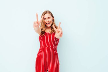 Son moda kırmızı tulum içinde gülümseyen güzel bir kadının portresi. Hippi kıyafetleri. Stüdyoda açık mavi duvarın yanında poz veren kaygısız seksi kadın. Pozitif model içeride eğleniyor. Neşeli ve mutlu.