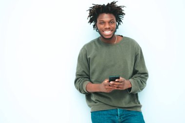 Yakışıklı, güler yüzlü, lamberseksüel model. Yaz kıyafetleri giymiş, traşsız Afrikalı adam. Stüdyoda mavi duvarın yanında poz veren, rastalı bir erkek. 