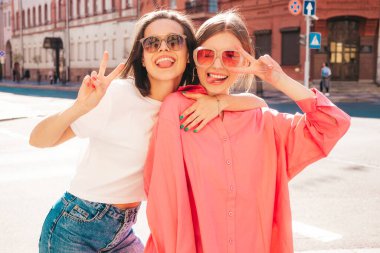 Son moda beyaz tişörtlü ve kot pantolonlu iki güzel, gülümseyen yeniyetme bayan sokak arka planında poz veren kaygısız kadınlar. Pozitif modeller eğleniyor, sarılıyor ve deliriyor.