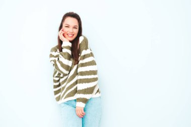 Yeni moda hippi kıyafetleri içinde gülümseyen güzel bir kadın. Stüdyoda açık mavi duvarın yanında poz veren kaygısız seksi kadın. Pozitif model içeride eğleniyor. Neşeli ve mutlu