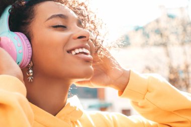 Afro kıvırcık saçlı güzel bir zenci kadın. Sarı kapüşonlu bir model. Kaygısız bir kadın. Kablosuz kulaklıkla müzik dinlemekten hoşlanıyor.