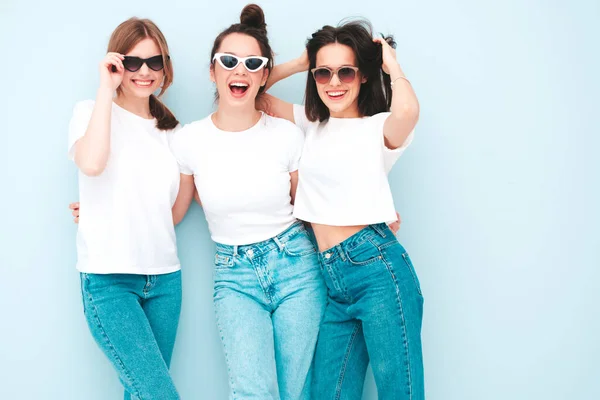 同じ夏の白いTシャツとジーンズの服で流行の3人の若い美しい笑顔のヒップスター女性 スタジオのライトブルーの壁の近くにポーズをとるセクシーな屈託のない女性 楽しさを持つ陽気で肯定的なモデル — ストック写真