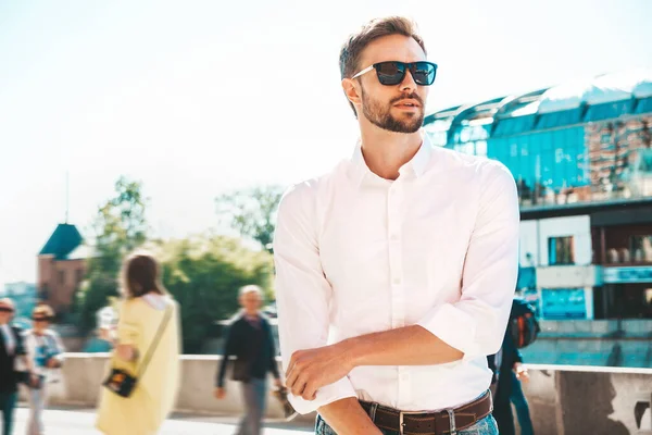 Yakışıklı, kendine güvenen, stil sahibi, Lambersex mankeni portresi. Beyaz gömlek giymiş modern bir adam. Sokakta güneş gözlükleriyle poz veren modacı erkek. Gün batımında dışarıda yürümek 