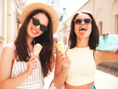 Son moda yaz kıyafetleri ve elbiseleri içinde gülümseyen iki güzel hippi kadın. Sokakta poz veren kaygısız kadınlar. Pozitif modeller gün batımında waffle külahında lezzetli dondurmalar yiyorlar.
