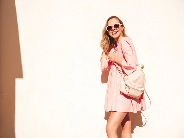 年轻美丽的嬉皮士女人穿着时髦的夏季粉色连衣裙 日落时分 一个性感无忧无虑的女人躺在街上的白墙边 带着手提箱的正面模特 快乐快乐 — 图库照片