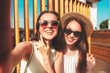Son moda yaz kıyafetleri içinde iki güzel gülümseyen yeniyetme kadın. Sokakta şapkalı kayla poz veren kaygısız kadınlar. Pozitif saf modeller gün batımında eğleniyorlar, Pov selfie çekiyorlar.