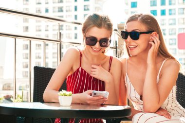 Moda yazında iki güzel, gülümseyen yeniyetme kadın. Kaygısız kadınlar, Veranda Kafe 'de sohbet ediyorlar. Model, arkadaşına akıllı telefonundan bilgi veriyor.