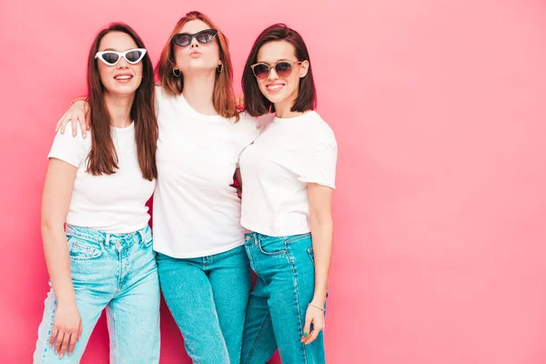 同じ夏の白いTシャツとジーンズの服で流行の3人の若い美しい笑顔のヒップスター女性 スタジオでピンクの壁の近くにポーズをとるセクシーな屈託のない女性 正のモデル — ストック写真