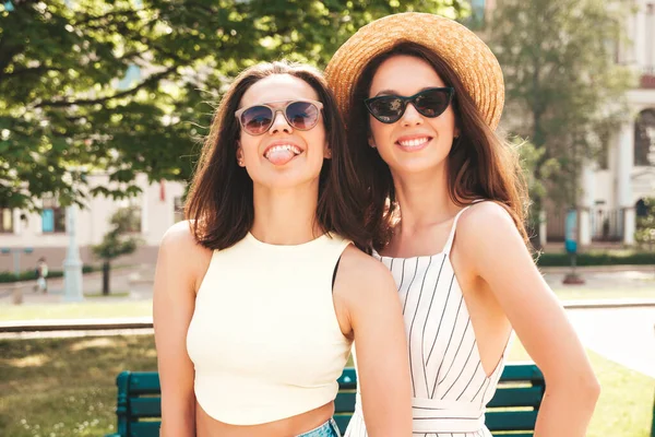 流行の夏服の2人の若い美しい笑顔ヒップスター女性 帽子の通りの背景にポーズ性的屈託のない女性 正の純粋なモデルは 日没で楽しみを持っています 抱擁と舌を示す — ストック写真