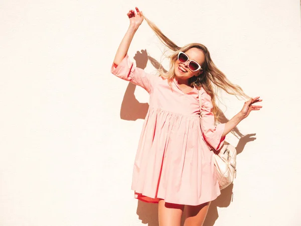 年轻美丽的嬉皮士女人穿着时髦的夏季粉色连衣裙 日落时分 一个性感无忧无虑的女人躺在街上的白墙边 带着手提箱的正面模特 快乐快乐 — 图库照片