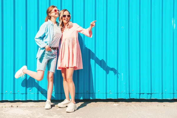 流行の夏の服やドレスで2人の若い美しい笑顔ヒップスター女性 ブルーの壁の近くの通りにポーズセクシーな屈託のない女性 — ストック写真