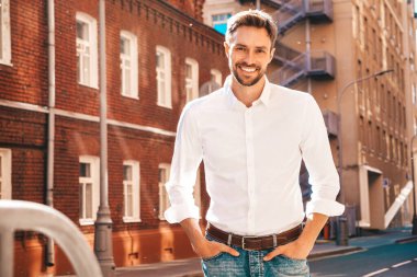Yakışıklı, gülümseyen stil sahibi Lambersex modelinin portresi. Beyaz gömlek giymiş modern bir adam. Sokakta poz veren düşünceli bir erkek. Gün batımında dışarıda. 