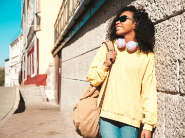 Afro kıvırcık saçlı güzel bir kadın. Sarı kapüşonlu bir model. Kaygısız bir kadın. Kablosuz kulaklıkla müzik dinlemekten hoşlanıyor.