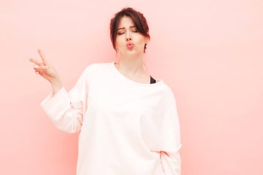 Yeni moda hippi kıyafetleri içinde gülümseyen güzel bir kadın. Stüdyoda pembe duvarın yanında poz veren kaygısız seksi kadın. Pozitif model içeride eğleniyor. Neşeli ve mutlu. Barış işareti nasıl?