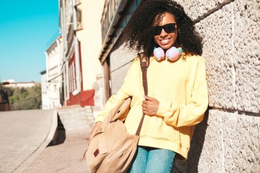 Afro kıvırcık saçlı güzel bir kadın. Sarı kapüşonlu bir model. Kaygısız bir kadın. Kablosuz kulaklıkla müzik dinlemekten hoşlanıyor.