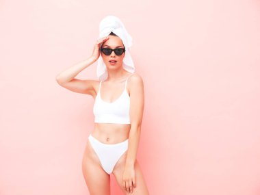 Beyaz iç çamaşırlı, gülümseyen genç bir kadın. İç çamaşırları ve kafasında havluyla stüdyoda pembe duvar pozu veren seksi tasasız manken. Pozitif ve mutlu bir kadın. Güneş gözlükleriyle sabahın tadını çıkarıyor.